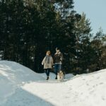 Couple enjoys winter walk with dog on snowy forest path.